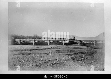 Un train traversant un pont au-dessus d'un lit de rivière asséché, avec des montagnes en arrière-plan, sur une photographie de la fin du XIXe siècle, faisant partie d'une collection documentant les travaux d'ingénierie civile dans les Pyrénées-Orientales, en Algérie, en Corse et dans le Var, en France. Banque D'Images
