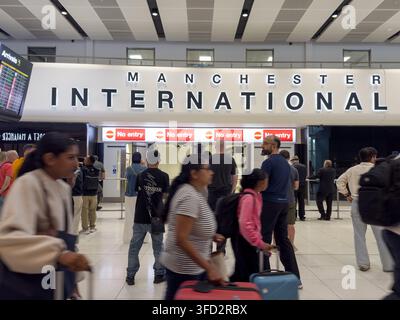Les voyageurs traversent le hall d'arrivée sous un grand panneau "Manchester International", Angleterre UK Banque D'Images
