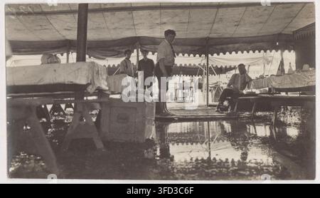 Un groupe de personnes associées au cirque Barnum et Bailey, debout sous une structure semblable à une tente près d'une zone inondée, lors d'un reportage photographique de 1906-1908. Banque D'Images
