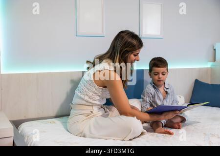 Mère et fils lisant un livre d'histoires sur le lit dans la chambre Banque D'Images