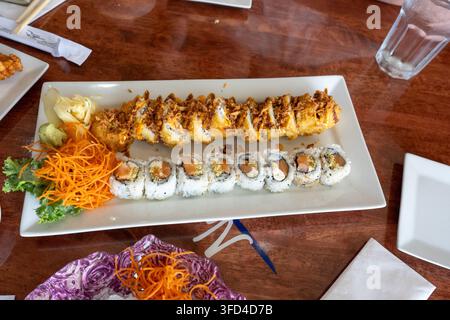 Grossissement de divers rouleaux de sushi servis sur une assiette rectangulaire blanche dans un restaurant japonais. Le plateau comprend des rouleaux au saumon, des sushi frits croustillants w Banque D'Images