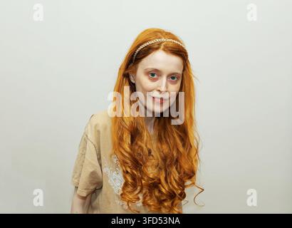 Jeune femme magnifique aux cheveux bouclés et roux souriant dans un intérieur domestique Banque D'Images