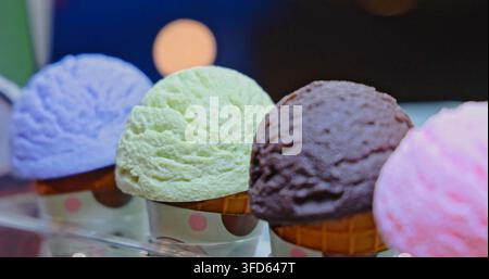 Boules de glace dans des cônes en gaufre exposées, différentes saveurs dont chocolat et menthe, arrière-plan d'intérieur de café, photographie commerciale de nourriture Banque D'Images