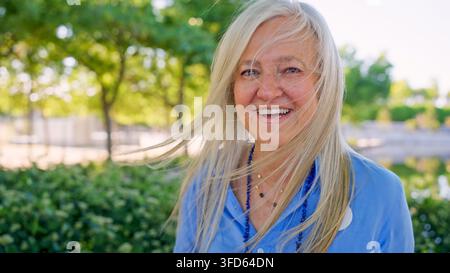 Femme âgée souriant avec ses cheveux soufflés par le vent en plein air dans un parc Banque D'Images