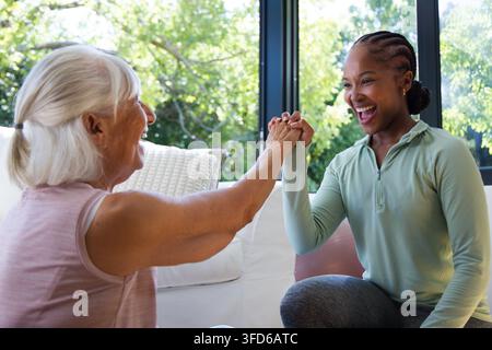 Sénior et entraîneur afro-américain en tenue de sport se serrant la main sur un canapé blanc dans le salon Banque D'Images