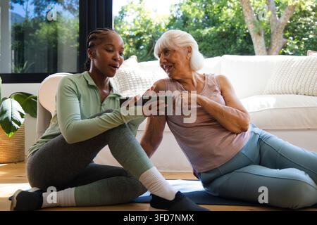 Entraîneur afro-américain en vêtements de sport tenant une tablette tandis qu'une femme âgée pointe sur des tapis sur un sol en bois Banque D'Images