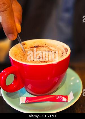 Cappuccino à la mousse épaisse dans une tasse en céramique rouge vif posée sur une soucoupe turquoise. Banque D'Images
