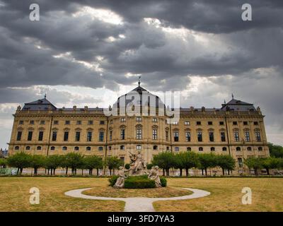 Wurtzbourg, Allemagne - 01 juil. 2026 : La grande résidence de Wurtzbourg à Wurtzbourg, en Allemagne, s'élève derrière une sculpture de jardin formelle sous des nuages orageux d'été dramatiques Banque D'Images