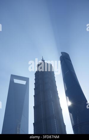 Vue en contre-plongée de la tour Shanghai, de la tour Jin Mao et des gratte-ciel SWFC devant un ciel bleu avec un rayon de soleil. Banque D'Images