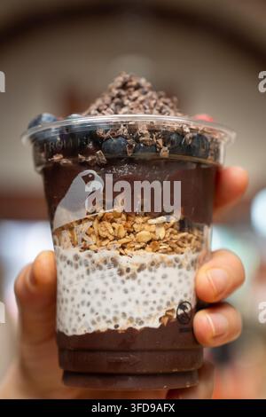 Une main tient une tasse à plusieurs couches de pudding à l'Açaí et aux chia Oakberry avec granola et myrtilles, savourant une collation saine et rafraîchissante. Banque D'Images