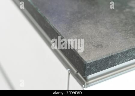 Une vue détaillée d'une surface en granit sombre polie avec des stries subtiles et un détail épuré d'une bordure métallique sur un fond blanc immaculé Banque D'Images
