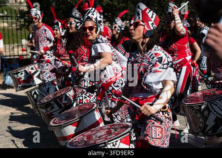 Une rangée dynamique de batteuses enthousiastes frappent activement leurs grands instruments de percussion avec des baguettes rouges tout en participant à une traditionnelle Banque D'Images