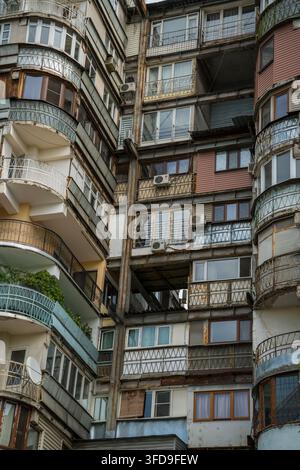 La façade érodée d'un immeuble d'habitation à plusieurs étages présente de nombreux balcons fermés et ouverts, certains avec des rampes en fer forgé ornées et oth Banque D'Images