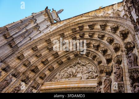 Vue ascendante d'un portail cathédrale gothique orné avec des arches en pierre profondément sculptées, des statues de saints et une scène en relief détaillée. Banque D'Images