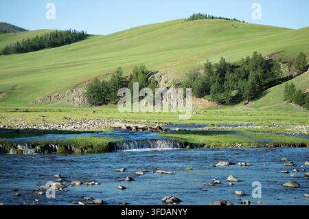 Vallée de l'Orkhon, Mongolie - 5 août 2026 : Un ruisseau cascade doucement devant une forêt de pins dans la vallée. Banque D'Images