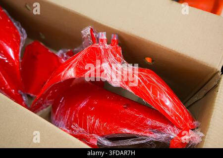 Un accessoire en plastique rouge emballé dans une boîte en carton, enveloppé dans un film de protection pour le stockage ou l'expédition Banque D'Images