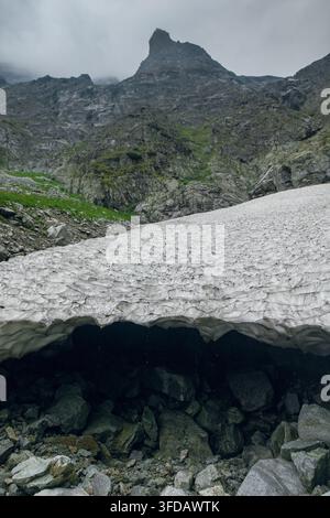 Un paysage montagneux escarpé dans les Tatras met en scène un pic aigu émergeant des nuages, avec une grande congère recouvrant les rochers en contrebas Banque D'Images