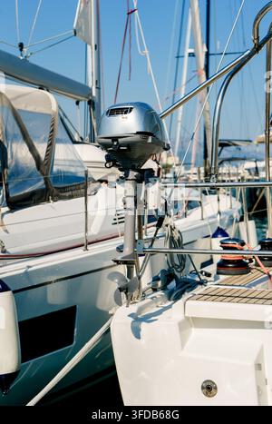Moteur hors-bord monté sur la poupe d'un voilier dans une marina moderne. Concept de transport maritime, de navigation, de maintenance et de voyage Banque D'Images