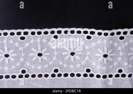 Ruban de dentelle florale blanc sur fond noir, bordure en coton brodé délicat. Vue de dessus motif de fleur à œillet brodé Banque D'Images