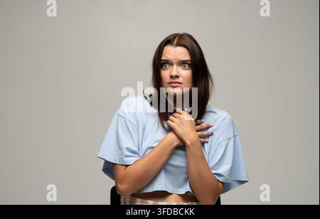 Jeune femme montrant de la peur et de l'anxiété, se sentant effrayée avec les yeux écarquillés et les mains pressant la poitrine Banque D'Images