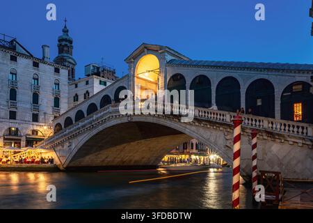 Pont du Rialto illuminé enjambant le Grand Canal à Venise, Italie, photographié pendant l'heure bleue le 19 juin 2026 avec des reflets lumineux sur les berges Banque D'Images