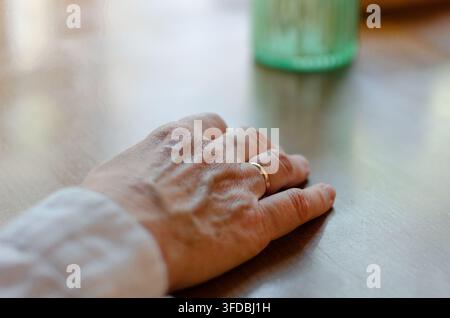 Gros plan d'une main portant une alliance reposant sur une table en bois Banque D'Images