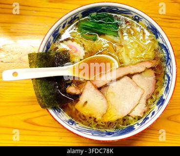 Un délicieux bol de ramen japonais traditionnel à la sauce soja, garni de porc chashu tendre, wonton, algues et épinards verts, servi dans une céramique décorative Banque D'Images