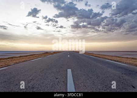 Une photo large en contre-plongée montrant une route asphaltée déserte qui traverse en ligne droite l'immense paysage plat du Chott el Djerid, en Tunisie, sous un Banque D'Images