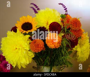 Un grand vase contient un mélange de fleurs comprenant des tournesols et des dahlias. L'arrangement présente des couleurs vives et divers types de fleurs. Cette scène tak Banque D'Images
