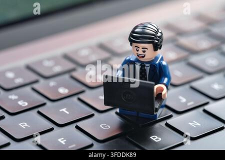 Tambov, Fédération de Russie - 29 août 2026 Une minifigure d'homme d'affaires Lego heureuse assise sur un clavier d'ordinateur tout en travaillant sur un ordinateur portable. Banque D'Images
