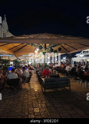 Des gens profitant d'une chaude soirée d'été, dînant et se relaxant sur la terrasse extérieure d'un restaurant en bord d'eau sous de grands parasols illuminés Banque D'Images
