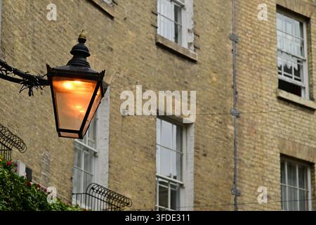Lampe de rue allumée sur support métallique, vieux bâtiment en briques et fenêtres en arrière-plan Banque D'Images