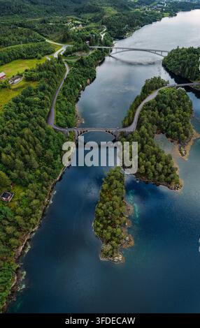 Perspective de drone du cours d'eau Straumen avec un pont en arc de pierre enjambant un canal étroit, une forêt de conifères dense couvrant les environs. Banque D'Images