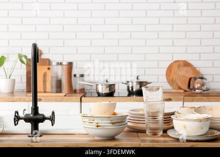 Ménages et épuisement domestique, pile de vaisselle sale et évier de cuisine en désordre après une soirée avec un tas d’assiettes et de bols non lavés Banque D'Images