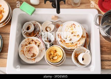Tâches ménagères et épuisement, pile de vaisselle sale dans l'évier de la cuisine avec des restes de nourriture et des taches de café après un repas Banque D'Images