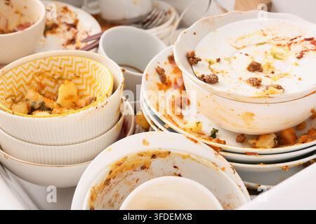 Ménages domestiques et désordre domestique, pile de vaisselle sale et bols graisseux dans l'évier de la cuisine après un dîner avec des restes de nourriture et des déchets alimentaires Banque D'Images