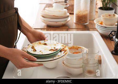 Ménages et farde domestique, personne lavant la vaisselle sale dans l'évier de la cuisine après un dîner avec des assiettes et des bols sales empilés pour le nettoyage Banque D'Images