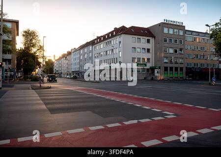 Large intersection urbaine avec des voies cyclables rouges et des bâtiments résidentiels et commerciaux mixtes sous la lumière du petit matin. Banque D'Images