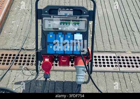 Boîte de distribution électrique portable avec plusieurs prises de courant industrielles bleues et rouges et câbles robustes installés sur une surface urbaine pavée à C Banque D'Images