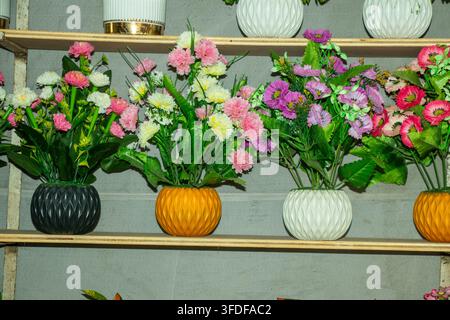 Vue rapprochée de plantes fleuries artificielles dans des vases multicolores élégants, soigneusement organisés sur des étagères d'exposition pour la décoration intérieure. Banque D'Images
