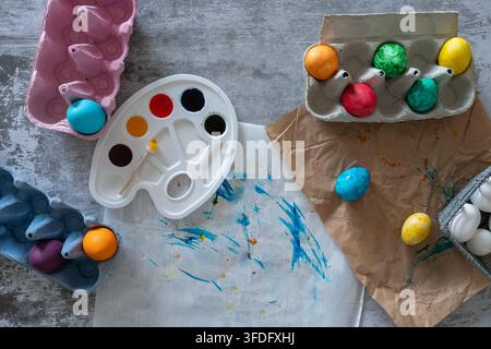 Composition artisanale de Pâques en vue aérienne mettant en avant des œufs décoratifs colorés, une palette d'aquarelle, des pinceaux et des matériaux d'artisanat supplémentaires disposés sur un ru Banque D'Images