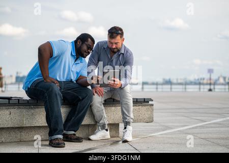 Deux hommes divers regardant une tablette en plein air Banque D'Images