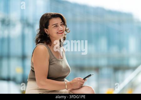 Femme mûre souriante tenant un smartphone en ville Banque D'Images