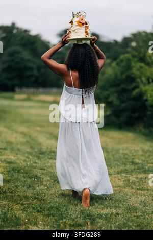 Une femme noire marche pieds nus en portant un gâteau sur sa tête Banque D'Images
