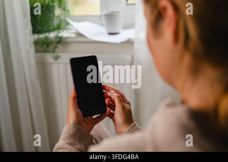 Vue par-dessus l'épaule d'une femme utilisant un téléphone à la maison Banque D'Images