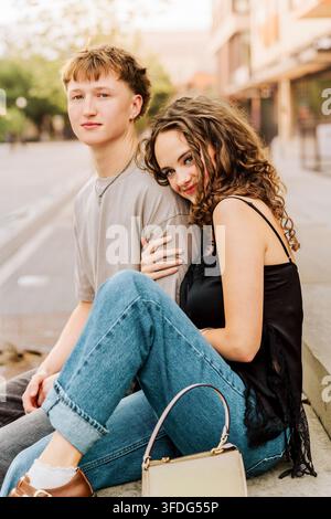 Jeune couple élégant assis ensemble sur un trottoir Banque D'Images