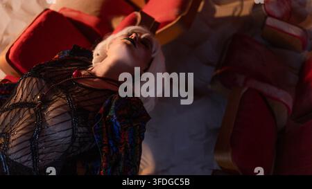 Un angle bas serré capture le visage tourné vers le haut et vers l'extérieur, baigné dans une lumière rouge, les couches texturées du costume remplissant le cadre avec un emo théâtral brut Banque D'Images