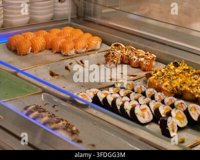 Prise de vue en hauteur d'un comptoir buffet de sushi coloré présentant des nigiri au saumon frais, des rouleaux maki et des rouleaux spécialement enrobés disposés soigneusement sur un plateau de service Banque D'Images