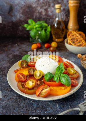 Salade fraîche de tomates et burrata avec des tomates colorées tranchées et du basilic servie dans une assiette Banque D'Images