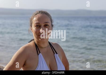 Une femme détendue se tient sur une plage en Croatie avec une mer calme et des collines lointaines en arrière-plan. Banque D'Images